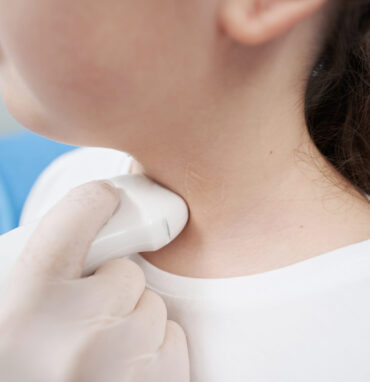 Endocrinologist using an ultrasound probe to examine the thyroid gland of young girl sitting in the office
