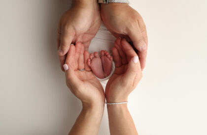 The palms of the parents. A father and mother hold the feet of a newborn child in a white blanket on a white background.. The feet of a newborn in the hands of parents. Photo of foot, heels and toes.